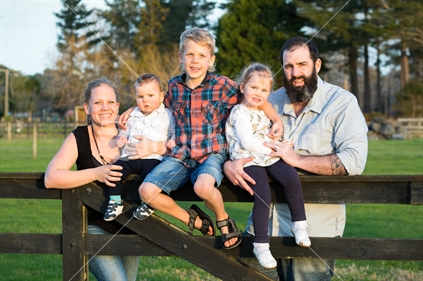 Happy family sitting on wooden farm gate
