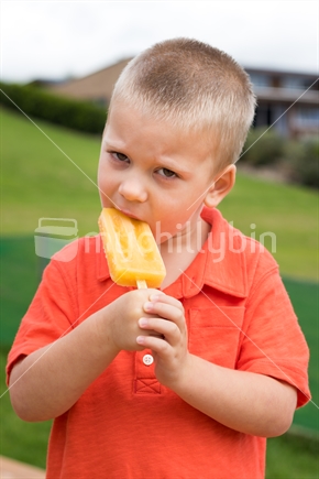 Little boy eating orange ice block
