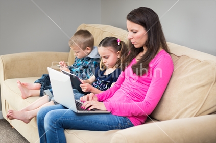 Mother And Children Using Digital Devices On Couch