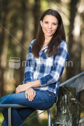 Beautiful woman sitting on farm gate