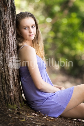 Blond teen girl sitting against tree