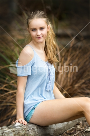 Pretty blond girl sitting on log in bush