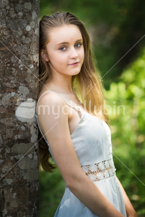 Beautiful blond girl leaning against tree