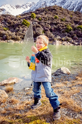 Boy holding sheet of ice by frozen lake