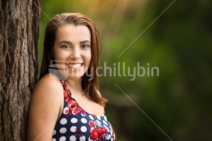 Pretty smiling woman leaning against tree