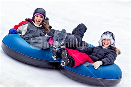 Friends riding tube down snow covered hill