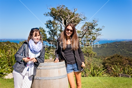 Two women drinking wine by wine barrel