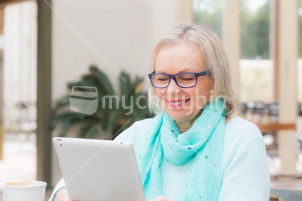 A 60 year old woman operates tablet computer at outdoor cafe