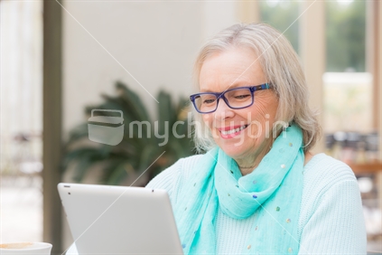 A blonde good looking middle aged woman sits at outdoor cafe with a tablet computer.