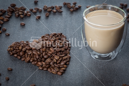 Heart shaped coffee beans, with coffee in glass mug.
