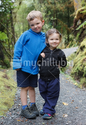 Brother and sister standing on a track in the bush.