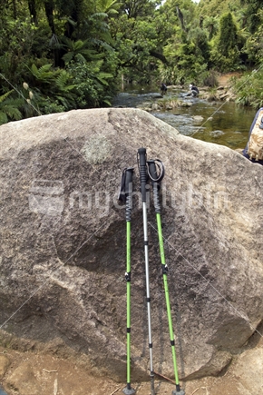 Walking Poles at rest by river, with people in the distance; Waiwera waterfall New Zealand