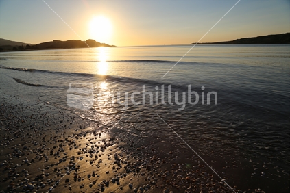 Raglan beach at sunset with the sunlight hitting the water and sand.