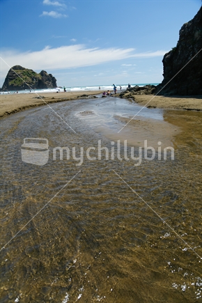 A stream of water going into the sea with land and sand.  Taken on Piha beach in Auckland.