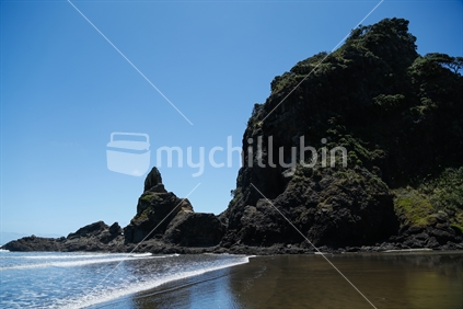 The rock formations on Piha beach in Auckland.  With the sky, sea and sand.